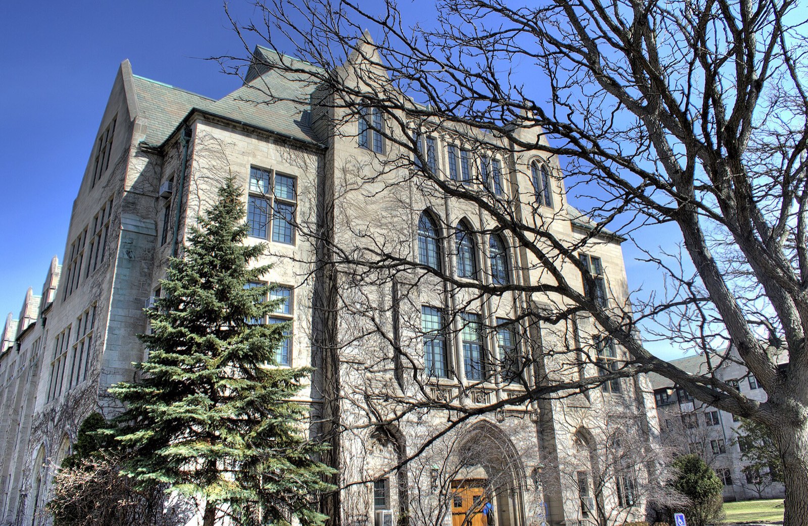 A gothic stone college hall behind bare winter trees